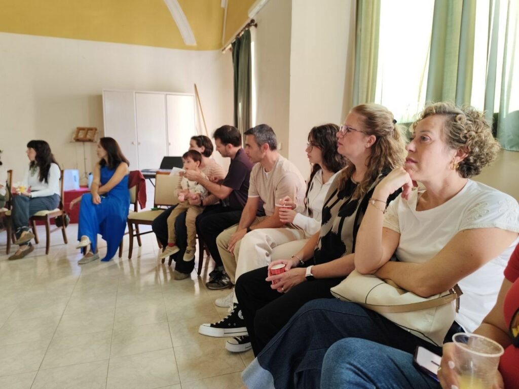 Hombres y mujeres sentados en círculo atendiendo a la reunión con un niño en brazos.