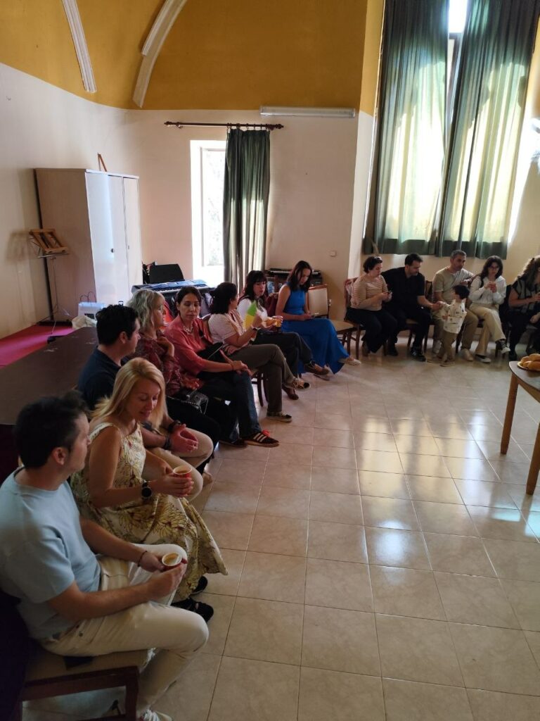 Varios adultos sentados en fila sosteniendo vasos en una reunión parroquial.