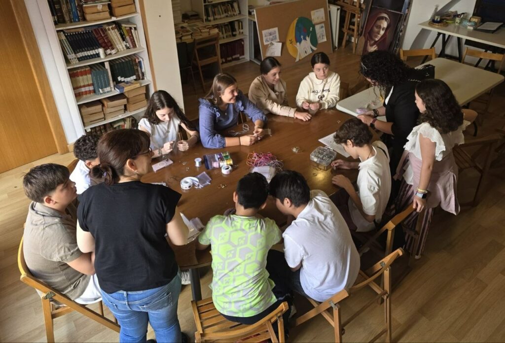 Jóvenes y catequistas sentados alrededor de una mesa de madera realizando un taller.